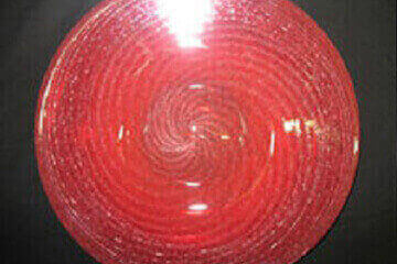 A red-pinkish memorial glass plate radiates concentric circle ridges illuminated with a textured appearance against a black background. It is used to honor the memory of a special pet.